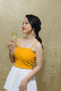 party, drinks, holidays, luxury and celebration concept - smiling woman in evening dress with glass of sparkling wine over gold background.