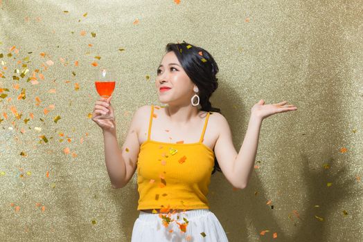 Beautiful young woman with confetti, celebration  with glass of champagne over gold background.