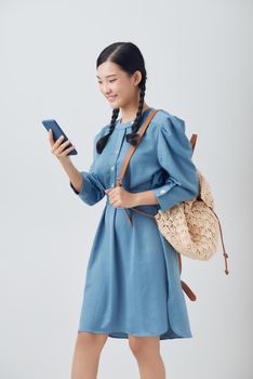 Studio shot of young happy Asian woman smiling while using mobile phone