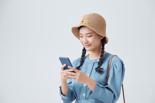 Fashion smiling woman using smartphone wearing straw hat over white background,