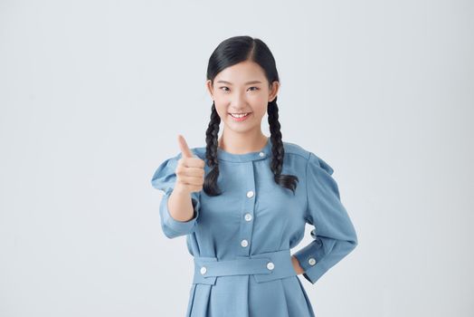 Excited pretty asian teenager holding thumbs up isolated over white background. Concept of positive evaluation.