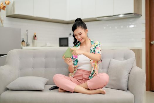 Smiling young asian woman using mobile phone app playing game, relax on sofa.