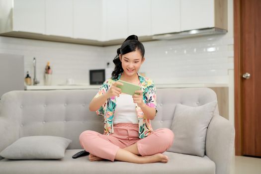 happy young woman on couch hold smartphone shop online or check mobile application or social media