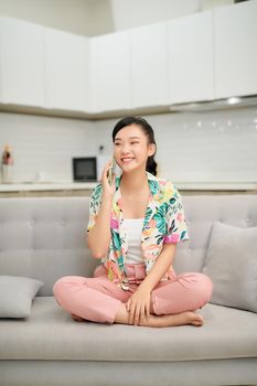 Happy young woman talking mobile phone while relaxing on couch