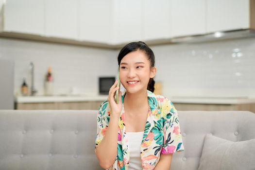 Pleasant talk with friend. Attractive smiling young redhead woman talking on cell phone while sitting on the beige sofa at home