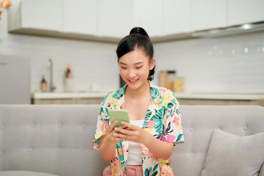 Happy millennial hispanic teen girl checking social media holding smartphone at home. 