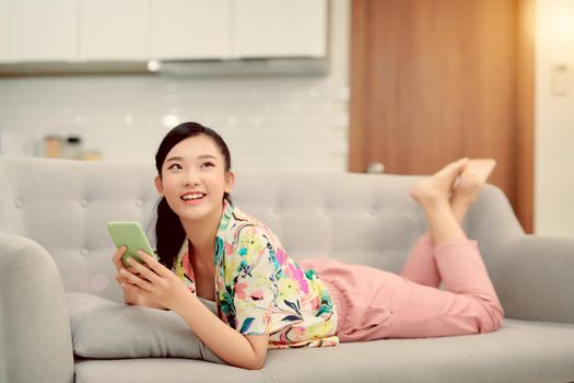 Asian woman reading text on couch at home in the living room