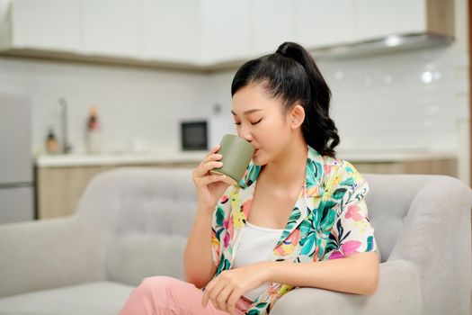 A woman looking to the side with a mug in her hands as she smiles and sits on the couch.