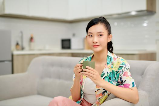 Young woman resting on couch and drinking tea in light room