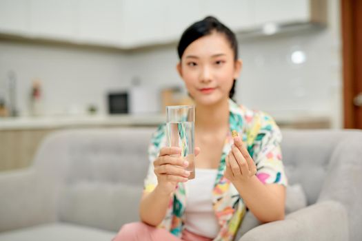 Happy woman taking a vitamin yellow pill sitting on a couch in the living room at home