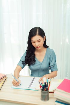 Focused school girl studying with books preparing for test exam writing essay doing homework at home