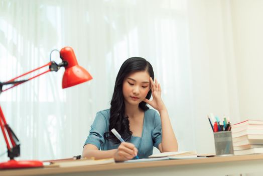 A young female student sitting at the table, using tablet when studying.