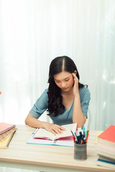 Focused millennial girl studying, preparing for entrance exams or university tests, reading book, taking down notes in textbook.