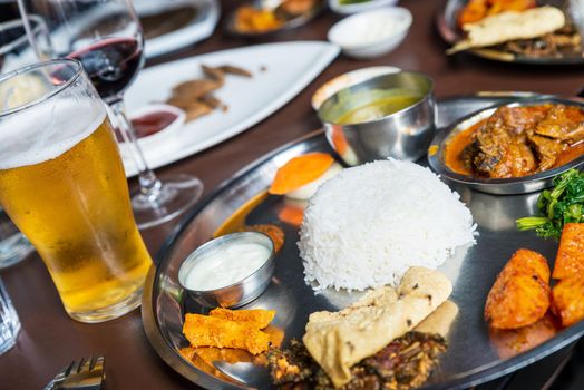 Traditional Nepali thali or dal bhat in restaurant with beer and wine glasses, in Kathmandu, Nepal