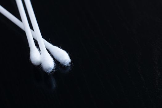 Three cotton buds on a black wooden table, copy space