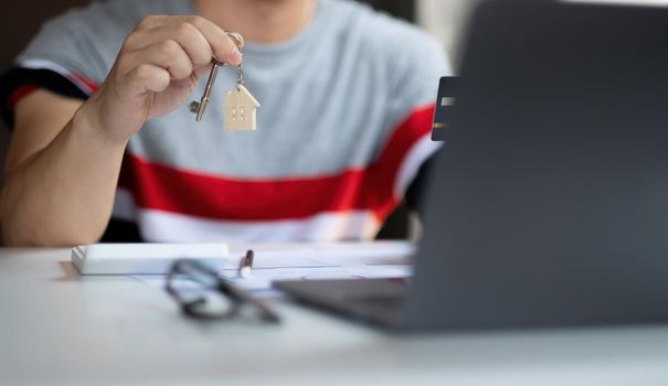 Real estate agent holding house key on table with house designs document,calculator,model house.Concept for real estate