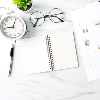 Top view of office table desk work concept with blank notebook, report, alarm clock on marble white background, concept of timing management and schedule planning.