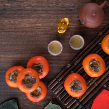 Top view of fresh sweet persimmons kaki with leaves on wooden table background for Chinese lunar new year fruit design concept, the word means blessing is coming.