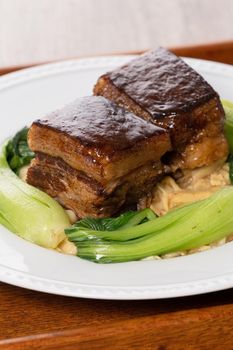 Dong Po Rou (Dongpo pork meat) in a beautiful white plate with green vegetable, traditional festive food for Chinese new year cuisine meal, close up.