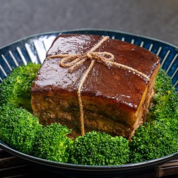 Dong Po Rou (Dongpo pork meat) in a beautiful blue plate with green broccoli vegetable, traditional festive food for Chinese new year cuisine meal, close up.