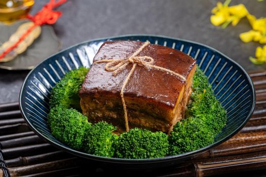 Dong Po Rou (Dongpo pork meat) in a beautiful blue plate with green broccoli vegetable, traditional festive food for Chinese new year cuisine meal, close up.
