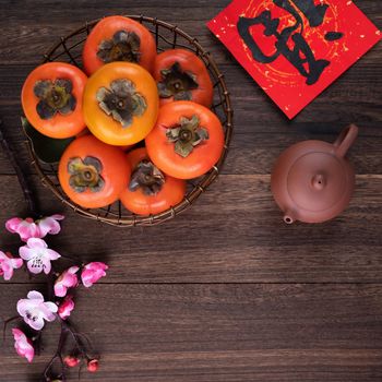 Top view of fresh sweet persimmons kaki with leaves on wooden table background for Chinese lunar new year fruit design concept, the word means blessing is coming.