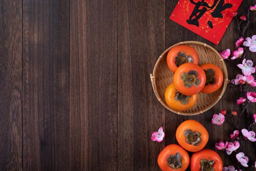 Top view of fresh sweet persimmons kaki with leaves on wooden table background for Chinese lunar new year fruit design concept, the word means blessing is coming.
