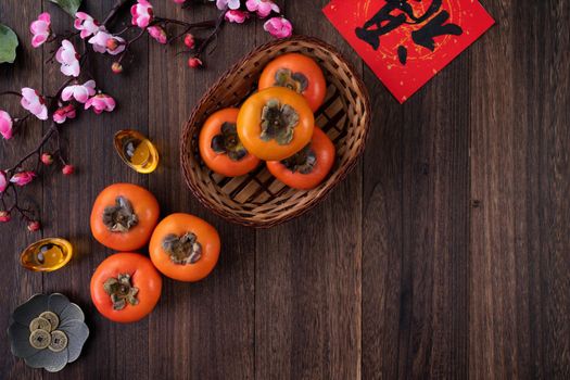 Top view of fresh sweet persimmons kaki with leaves on wooden table background for Chinese lunar new year fruit design concept, the word means blessing is coming.
