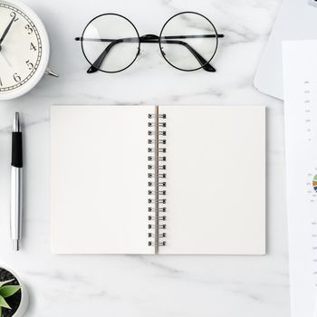 Top view of office table desk work concept with blank notebook, report, alarm clock on marble white background, concept of timing management and schedule planning.