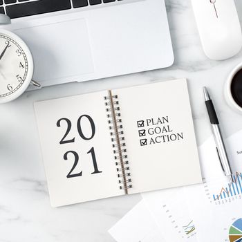 Top view of office table desk 2021 Goal work concept with keyboard, notebook, pencil, eyeglasses and coffee on bright marble white background.