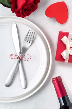 Empty white plate with tableware, ribbon, gift and roses for Valentine's Day special holiday dating meal concept.