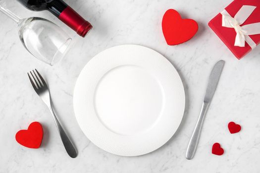 Empty white plate with tableware, ribbon, gift and roses for Valentine's Day special holiday dating meal concept.