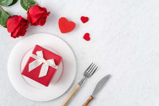 Empty white plate with tableware, ribbon, gift and roses for Valentine's Day special holiday dating meal concept.