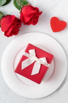 Empty white plate with tableware, ribbon, gift and roses for Valentine's Day special holiday dating meal concept.