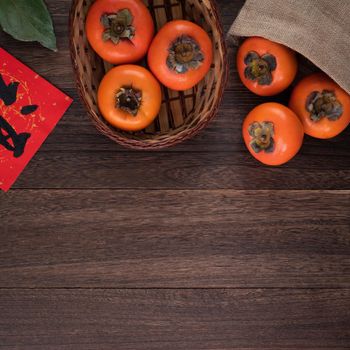 Top view of fresh sweet persimmons kaki with leaves on wooden table background for Chinese lunar new year fruit design concept, the word means blessing is coming.