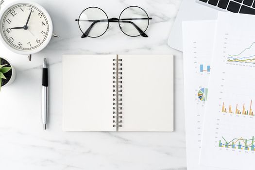 Top view of office table desk work concept with blank notebook, report, alarm clock on marble white background, concept of timing management and schedule planning.