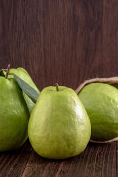Close up of delicious beautiful guava set with fresh green leaves isolated on dark wooden table background.