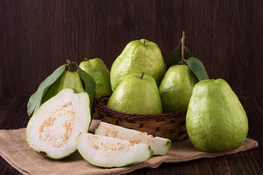 Close up of delicious beautiful guava set with fresh green leaves isolated on dark wooden table background.