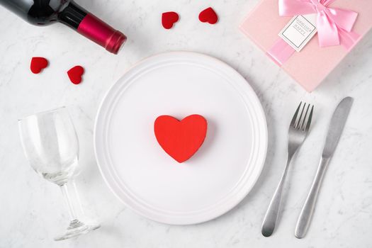 Empty white plate with tableware, ribbon, gift and roses for Valentine's Day special holiday dating meal concept.
