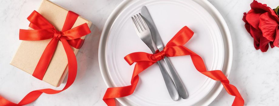 Empty white plate with tableware, ribbon, gift and roses for Valentine's Day special holiday dating meal concept.