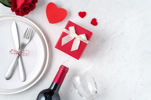 Empty white plate with tableware, ribbon, gift and roses for Valentine's Day special holiday dating meal concept.