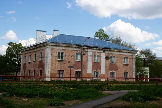 Two-story apartment building old red house with stucco walls against a blue sky with clouds.
