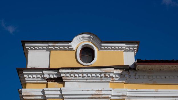 The facade with a round window of a yellow old house against a blue sky.