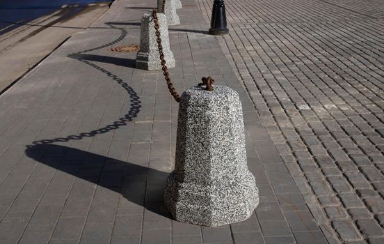 Granite pillars with a stretched black metal chain separate the sidewalk from the roadway.
