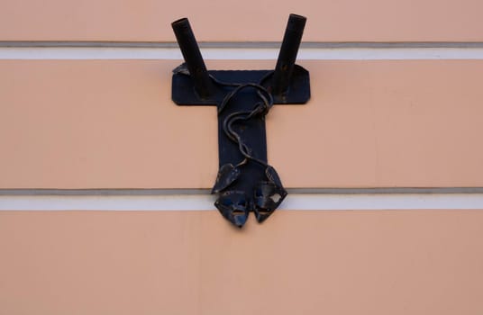 An antique metal forged rusty flagpole with decorative elements in the form of theatrical masks on the pink wall.