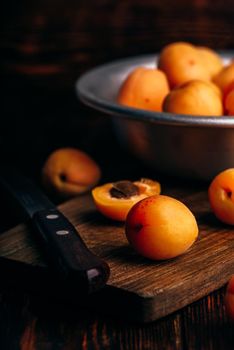 Mellow apricots with knife over old wooden cutting board and metal bowl with fruits