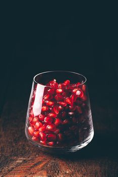 Glass full of red pomegranate seeds on wooden table