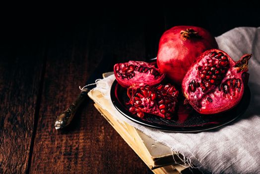 Open pomegranate fruit on metal plate over old books
