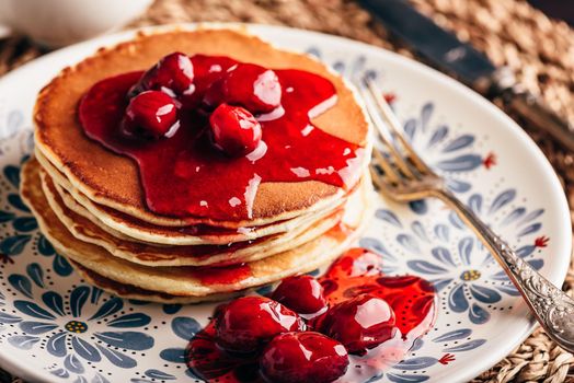 Stack of pancakes with dogwood berry marmalade on white plate with ornate