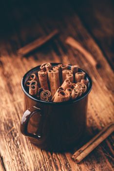 Cinnamon sticks in a metal mugr over rustic wooden surface